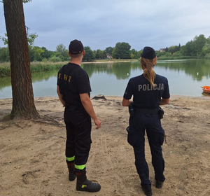 Policjantka umundurowana  oraz strażak umundurowany stoją nad zbiornikiem wodnym podczas patrolu.
